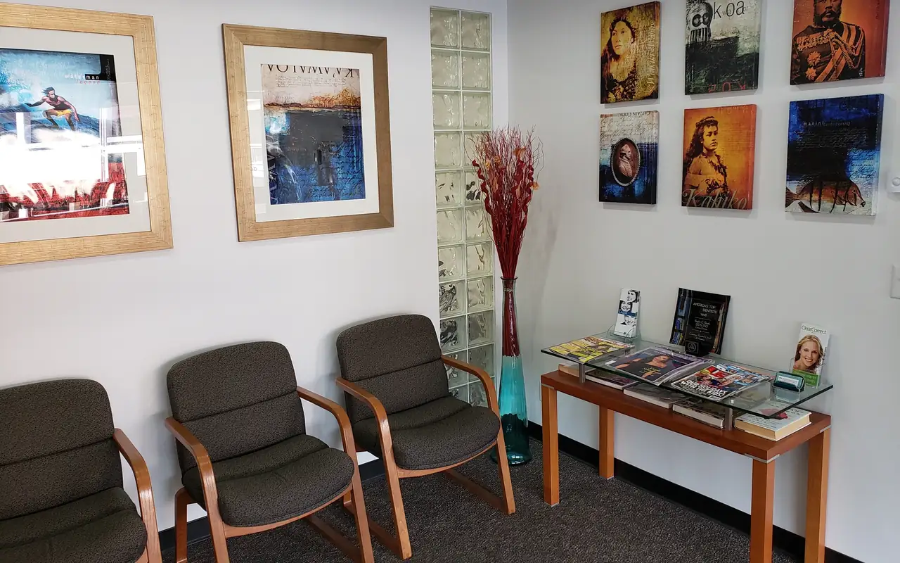 The waiting room at Hawaii Cosmetic Dental in Manoa Marketplace, with a wall of Hawaiian portrait art above a reading table.