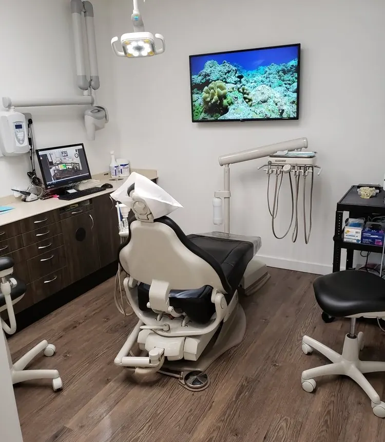 A treatment room at Hawaii Cosmetic Dental, with the dental chair, a monitor and a wall screen showing a coral reef.